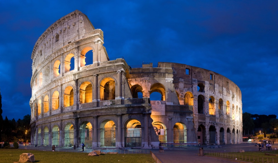 The Colosseum in Rome illuminated in gold against a deep blue evening sky